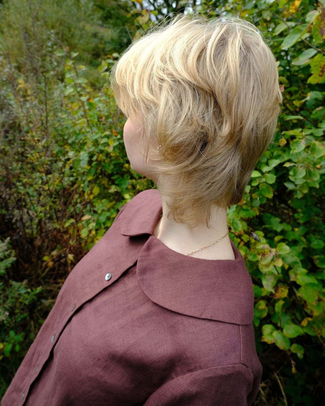 Person wearing a maroon shirt with a blurred natural background