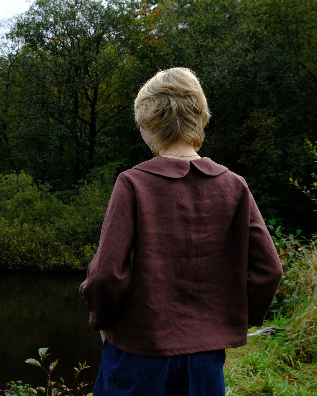Person wearing a maroon jacket standing in a forested area