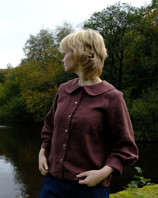 Person wearing a maroon shirt standing by a body of water with trees in the background