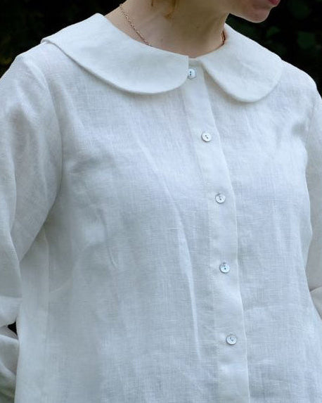 Woman wearing a white blouse with a Peter Pan collar against a dark background