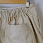 Beige pants hanging on a wooden hanger against a white background