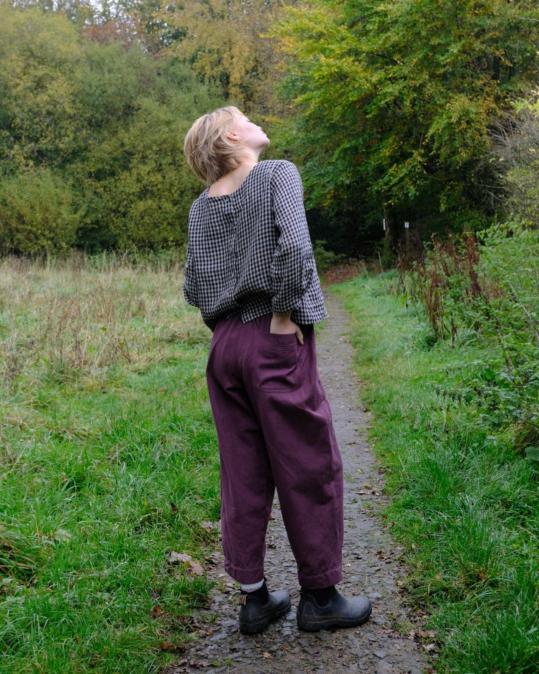 Person standing on a path in a natural setting with trees and grass.