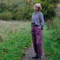 Person standing on a path in a natural setting wearing a checkered sweater and purple pants.