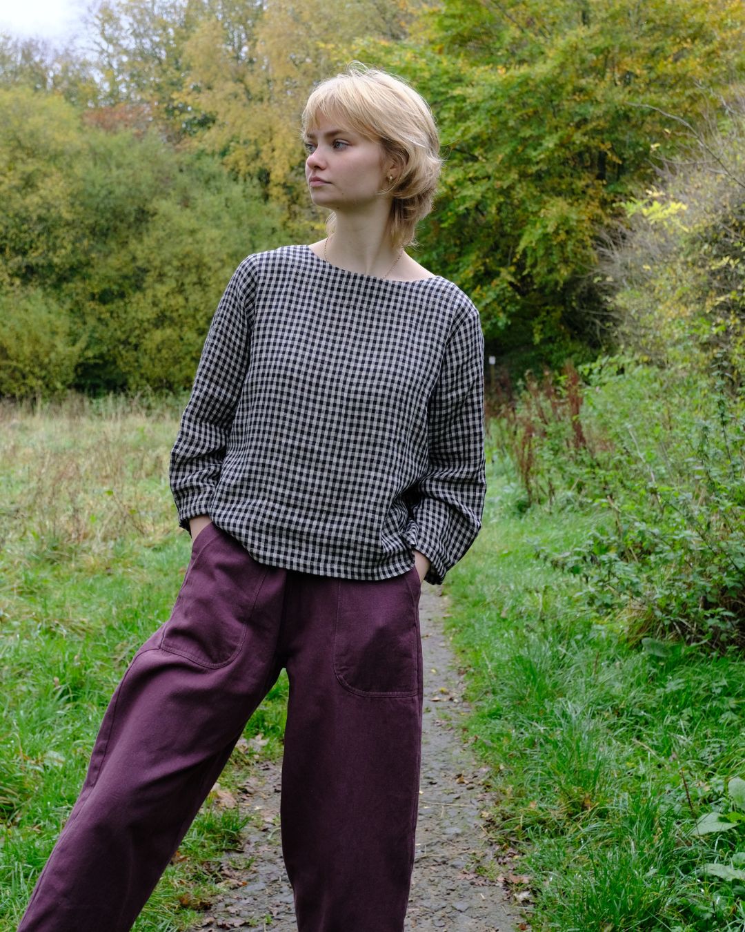 Woman wearing a checkered shirt and purple pants standing on a path in a natural setting