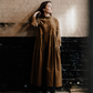 woman standing against a painted brick wall in a tiered brown corduroy dress.