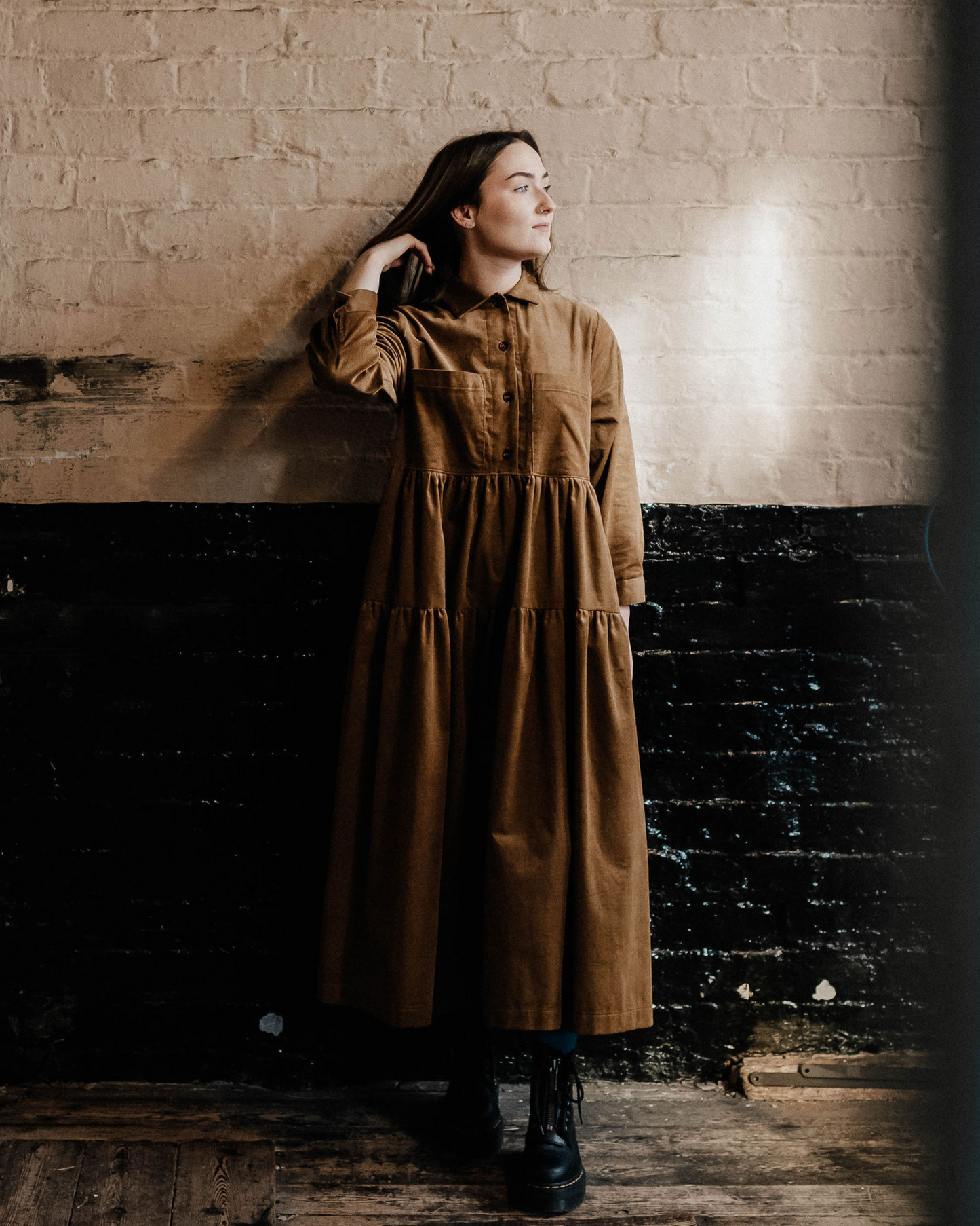 woman standing against a painted brick wall in a tiered brown corduroy dress.