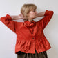 A person modeling a red needlecord shirt with patch pockets, a neat collar with a contrast floral print, and bracelet length sleeves finished with a cuff.