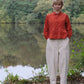 Person wearing a red jacket and white pants standing by a lake with trees in the background