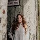 Woman standing against a rustic wooden wall with a sign above her.