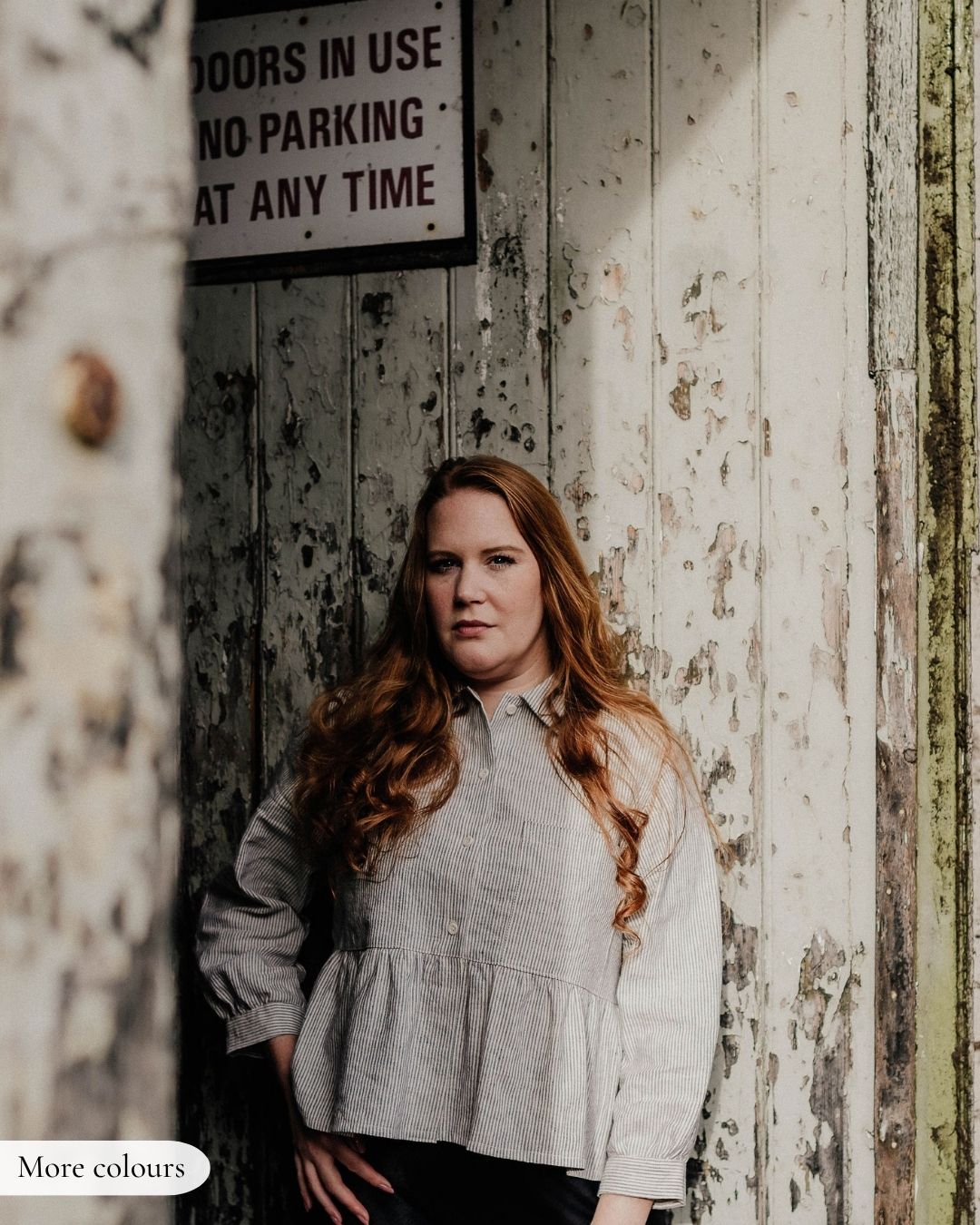 Woman standing against a rustic wooden wall with a sign above her.