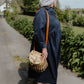 Woman in  Dorothy shirtdress Noah navy  blue with a straw bag walking on a path with greenery around.