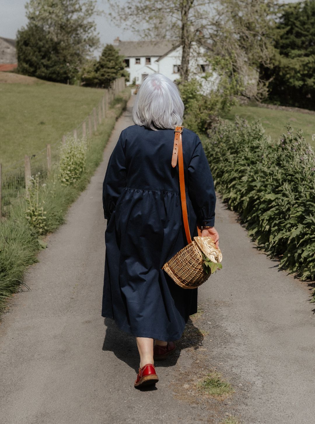 Person walking down a path in a rural setting with a basket and flowers.