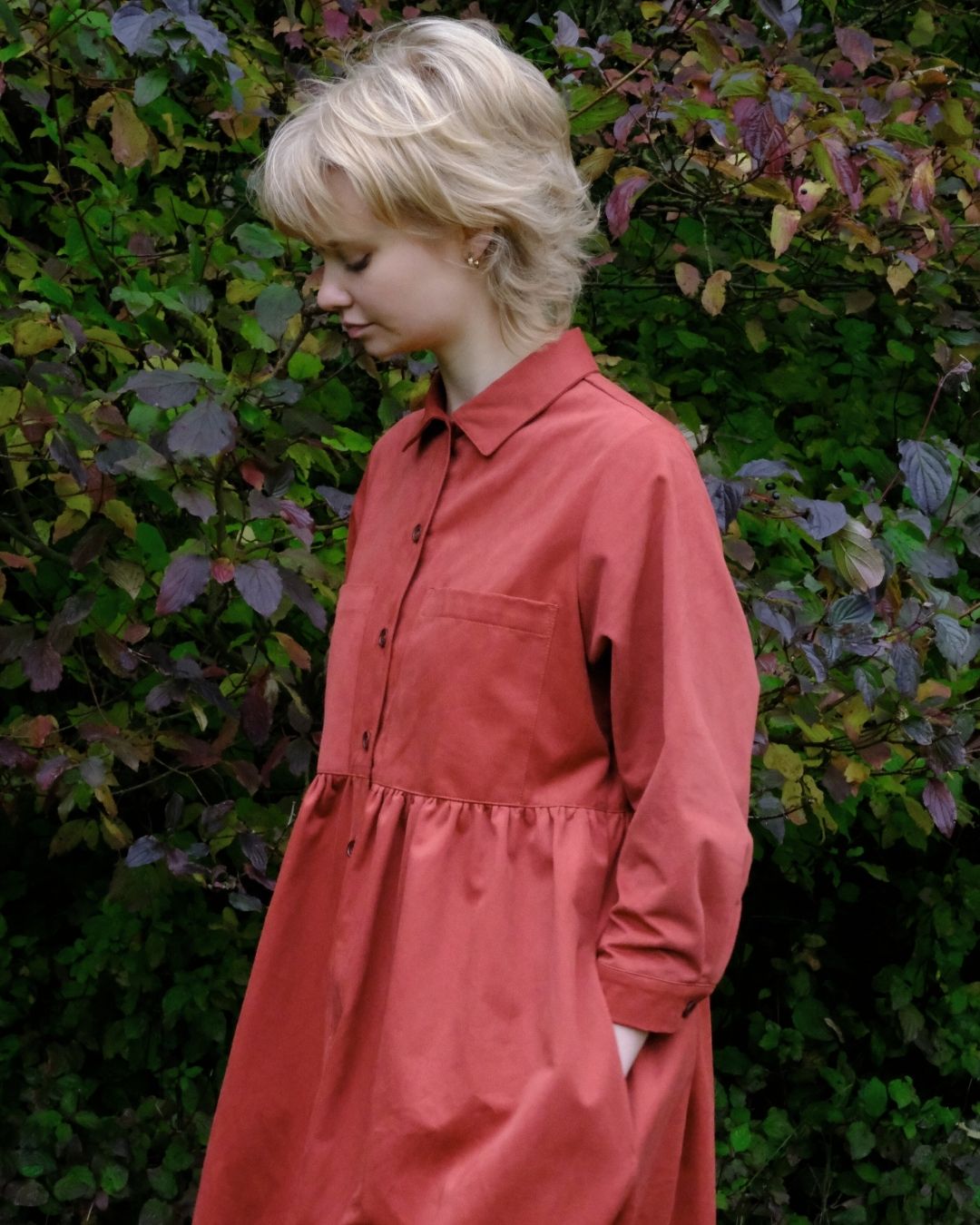 Woman wearing a red dress standing in front of green foliage