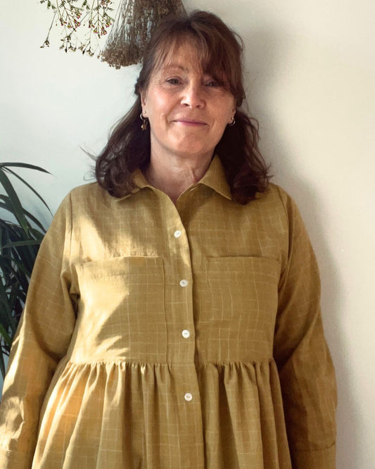 Woman wearing a mustard yellow dress against a white wall.