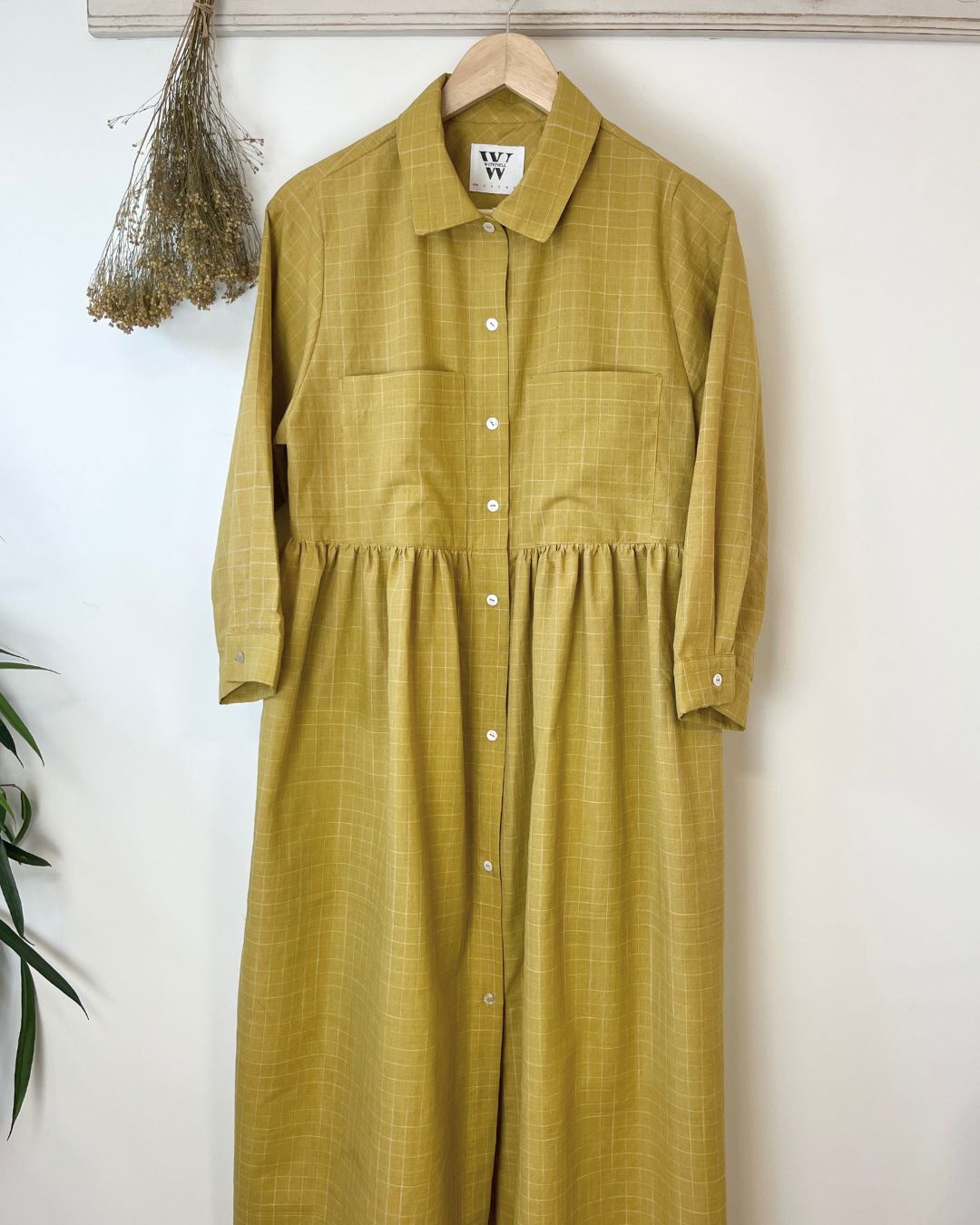 mustard checkered dress on a hanger against a white wall
