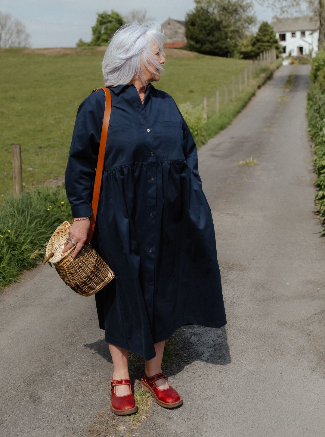 Woman in a  blue dress walking on a rural road with a basket.