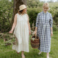 Two women in long dresses walking outdoors with baskets, surrounded by greenery.