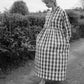 Woman wearing a checkered dress standing in a garden.