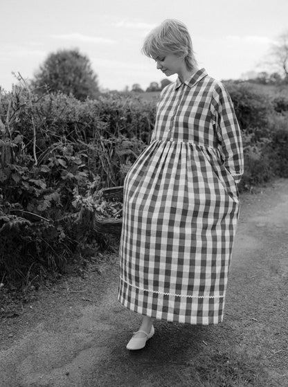 Woman wearing a checkered dress standing in a garden.