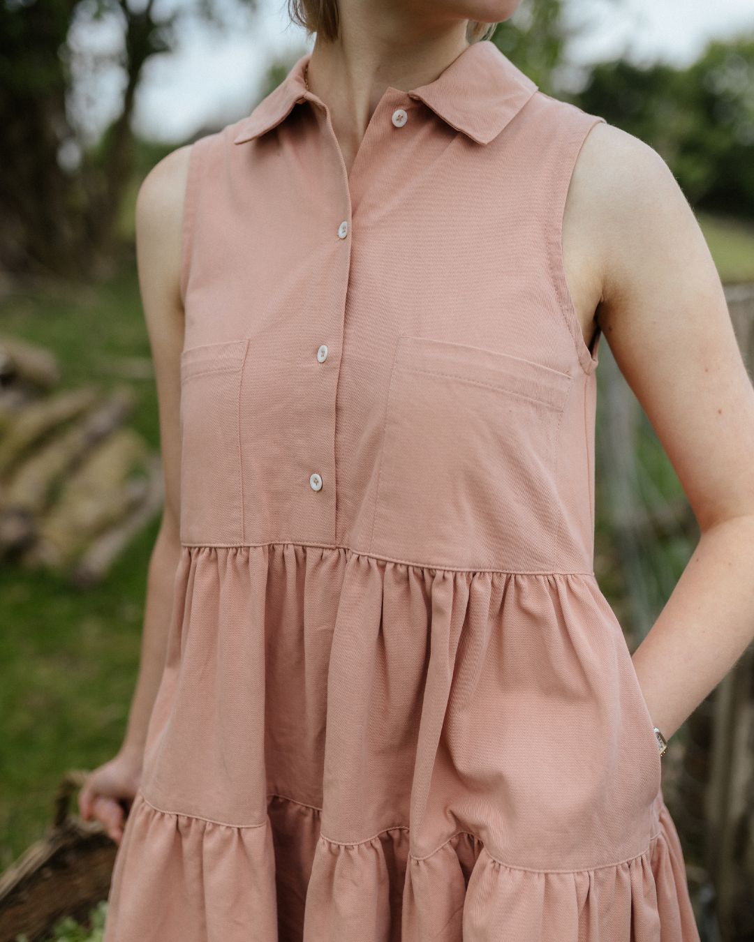 Cropped view of woman wearing sleeveless pink  dress with collar and 4 buttons to front