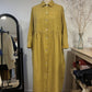 Yellow checkered dress on a mannequin against a white wall with a mirror and shelves in the background.