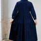 Person wearing a navy blue dress standing in a room with a white wall and wooden floor.