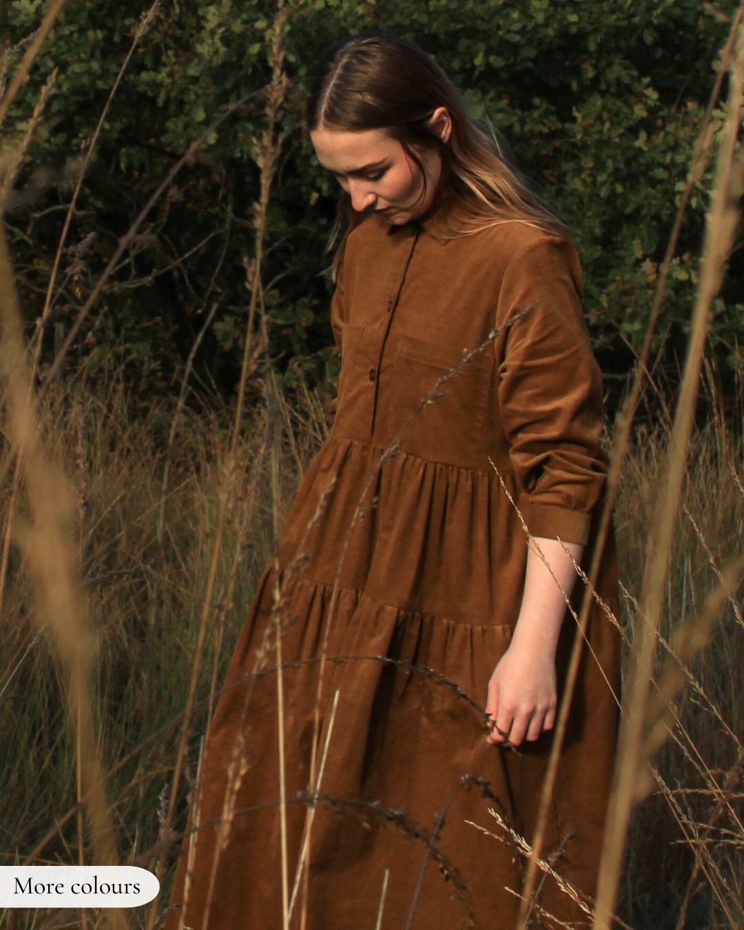 Woman in a brown dress standing in a field with tall grass and greenery.
