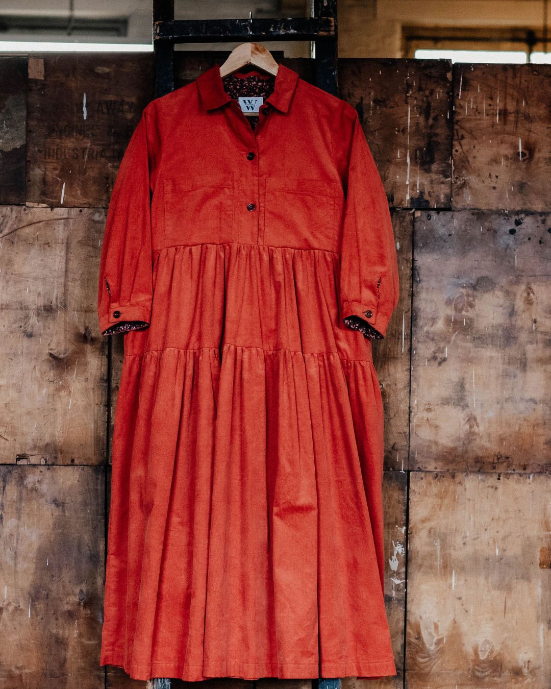 orange corduroy Dress hangiing on a ladder in a industrial setting.