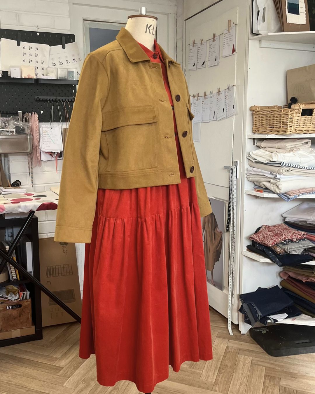Dress makers dummy with orange dress and brown jacket.