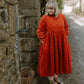 Woman in a red dress standing next to a stone wall with a wicker basket.