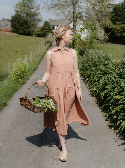 Woman in effie  pink dress holding a basket of flowers walking on a path in a garden.