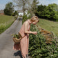 Woman in  pink dress standing on a rural road, holding a basket of plants.