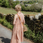 Woman in Effie pink dress walking along a country path with stone walls and greenery.