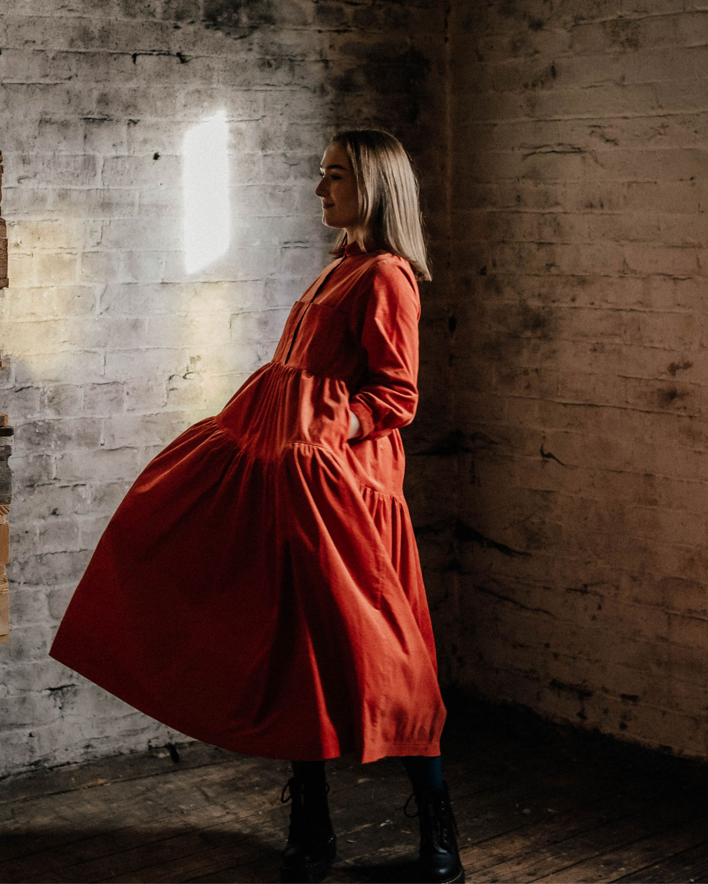 woman in an old factory wearing a orange corduroy dress with tiers.