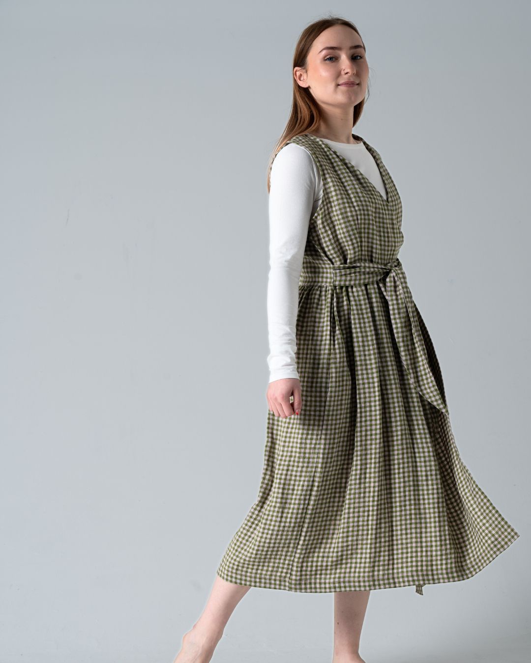 Woman wearing a green checkered dress over a white long-sleeve shirt on a gray background
