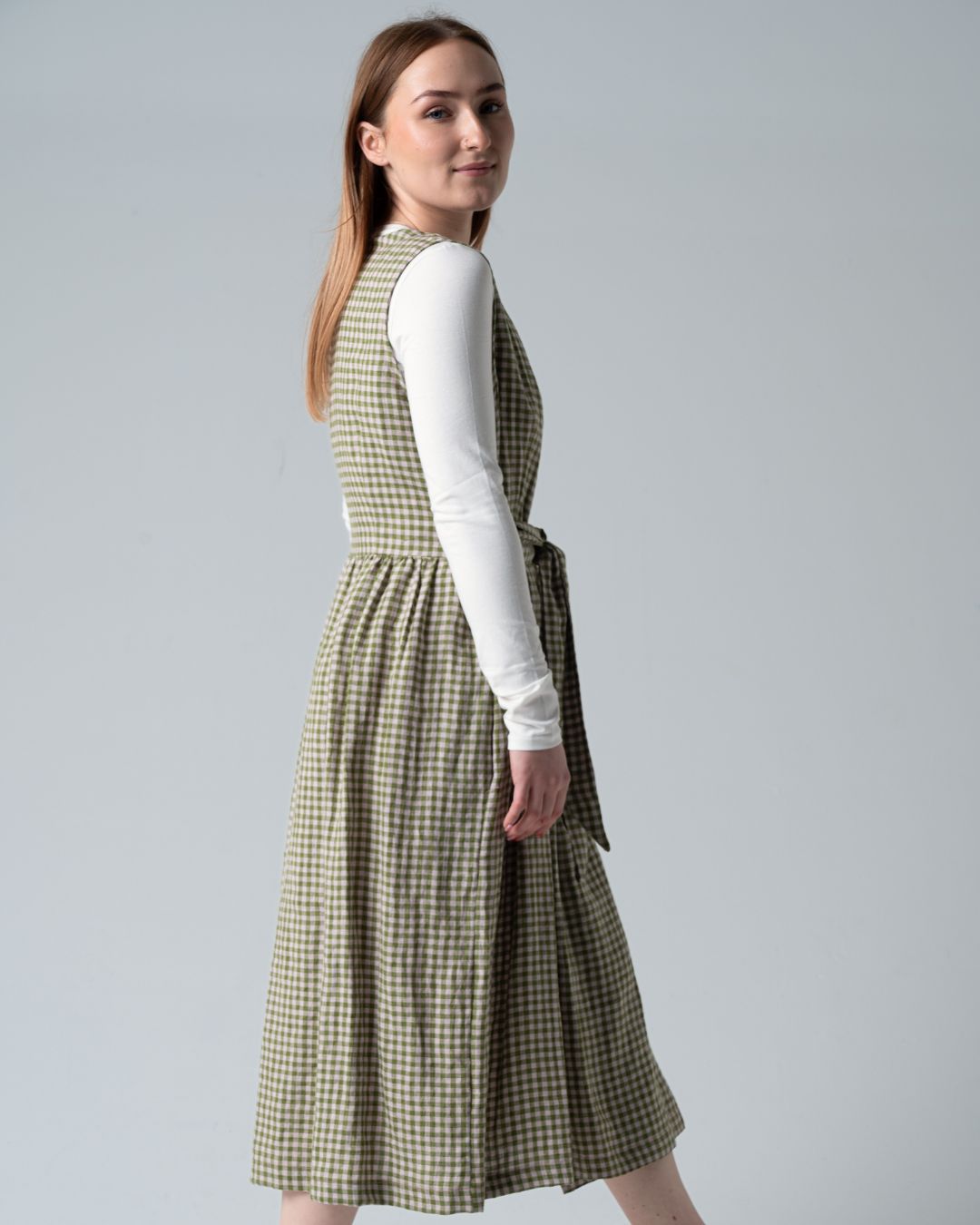 Woman wearing a green checkered dress over a white shirt on a gray background
