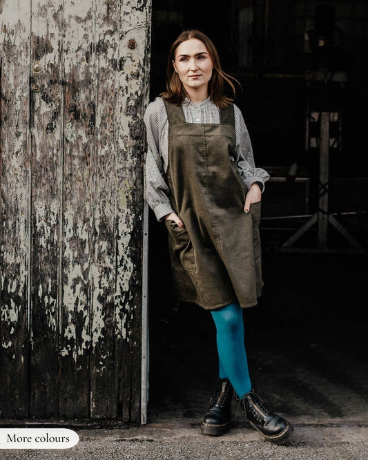 Woman wearing a brown apron standing in front of a rustic wooden door.
