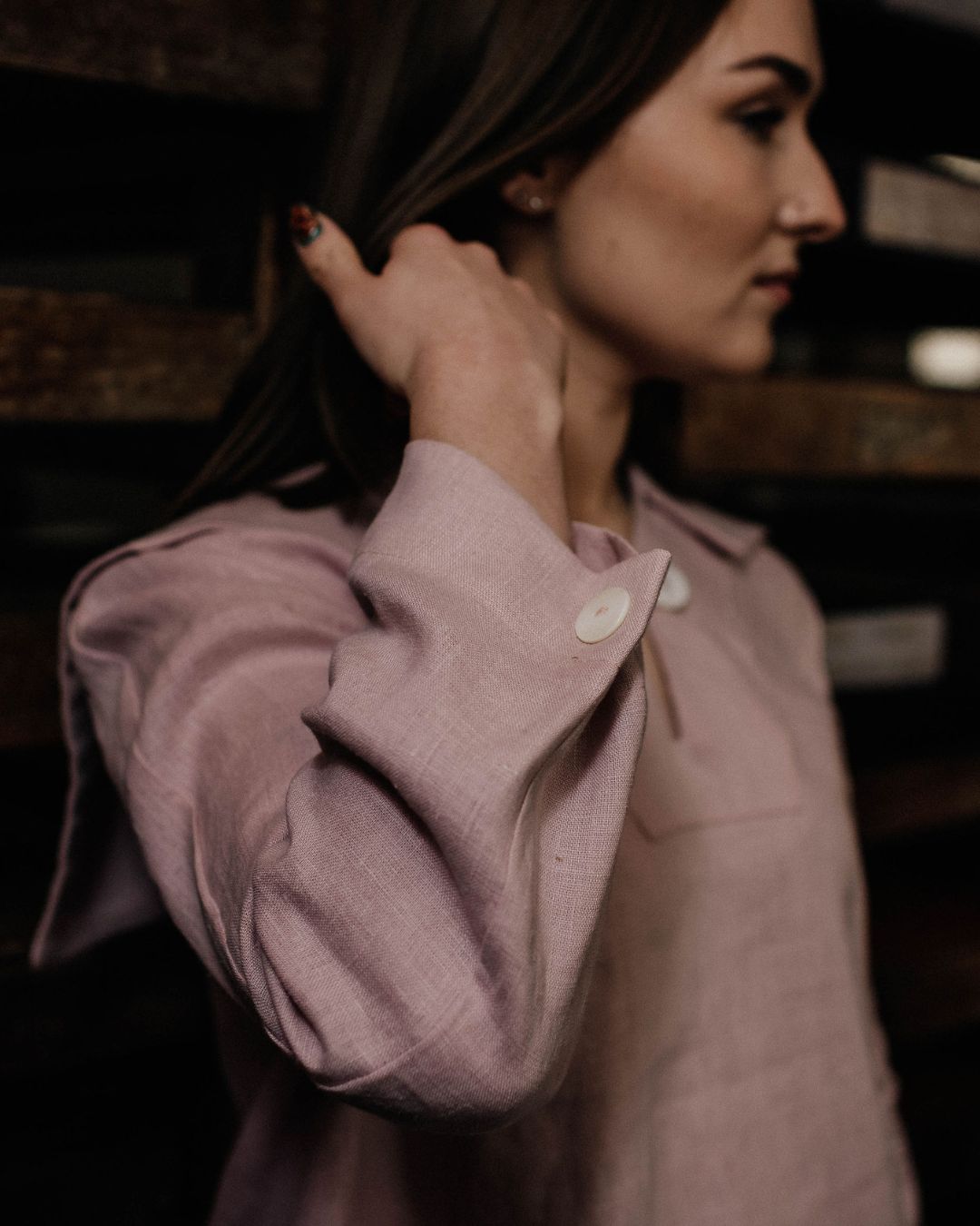 Woman wearing a light pink shirt with rolled-up sleeves in a dimly lit setting