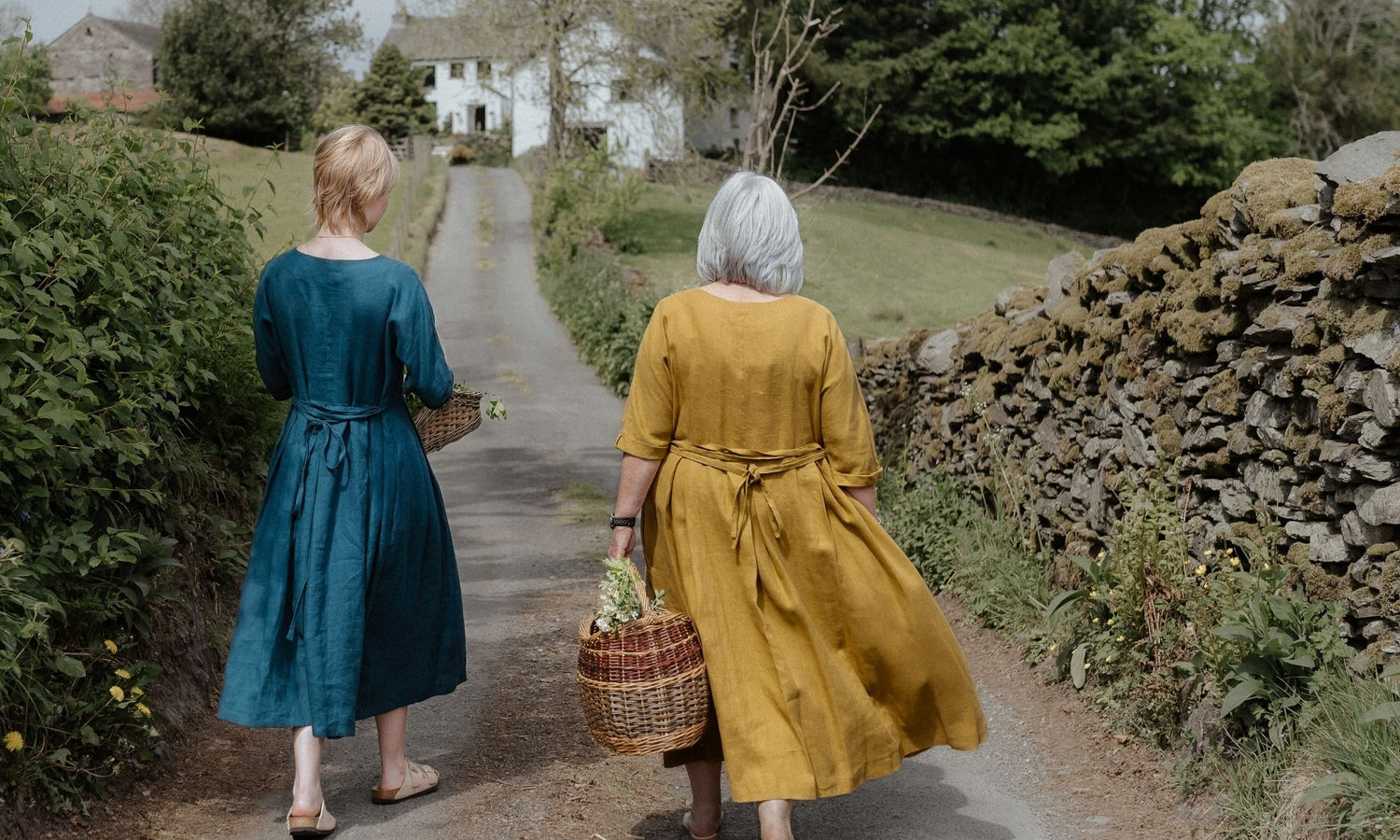 Two women walking along a path in a rural setting, one in a blue dress and the other in a yellow dress.