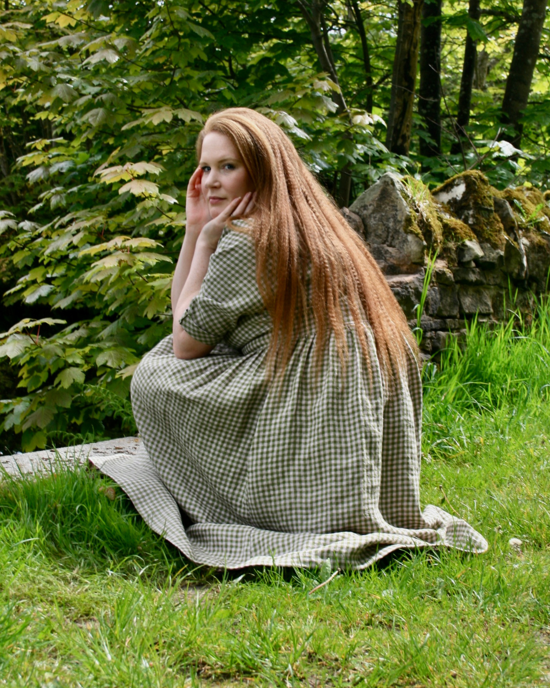 Woman sitting in countryside setting and wearing a green linen dress.