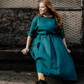 woman sitting on wall wearing a teal linen dress with tied waist.