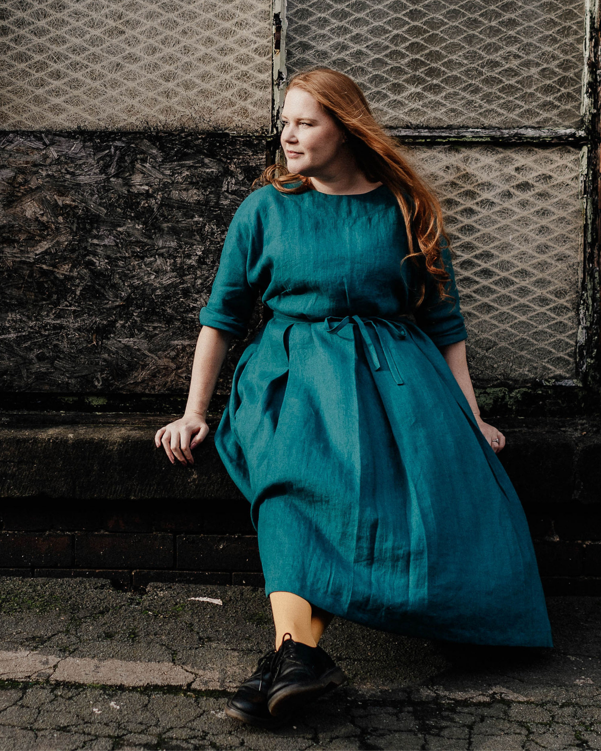 woman sitting on wall wearing a teal linen dress with tied waist.
