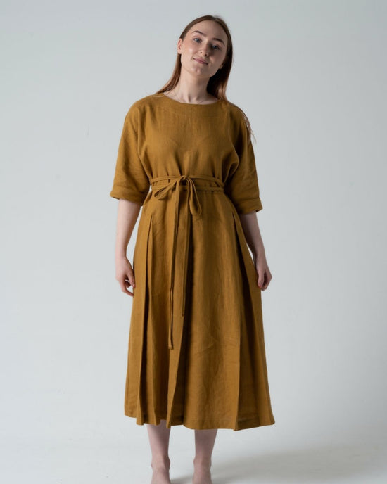 Woman wearing a mustard yellow dress against a white background