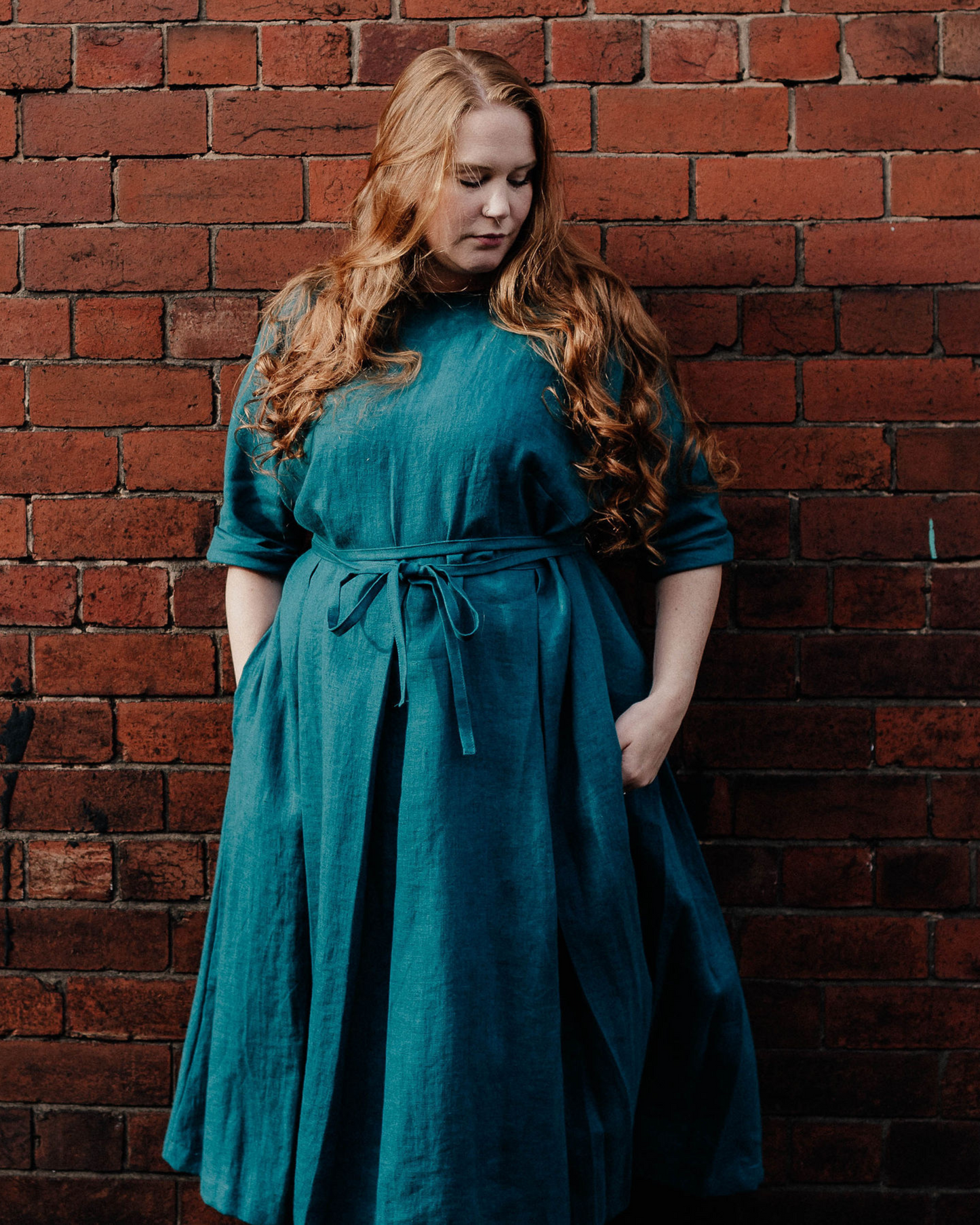 A model wearing a blue  linen dress with elbow length  sleeves, standing against a brickwall