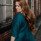 A model wearing a teal linen dress  and standing by  a brick building.