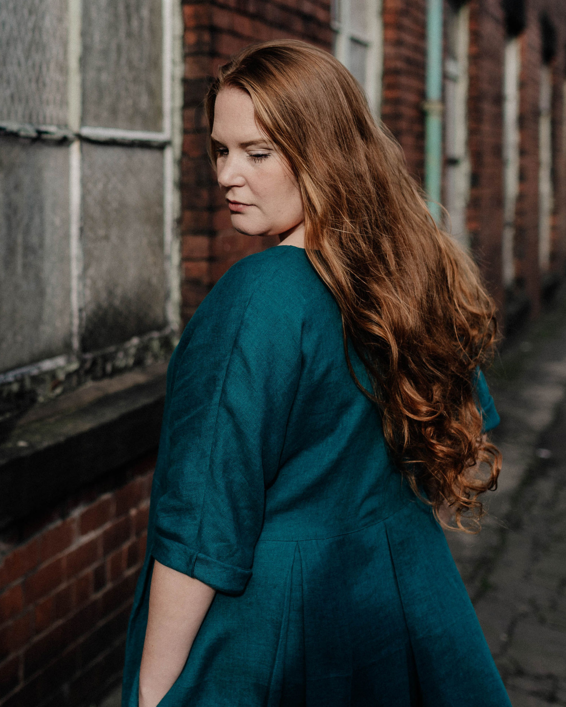 A model wearing a teal linen dress  and standing by  a brick building.