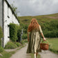 Woman with long red hair in a green dress walking away from a white building towards a grassy hill.
