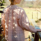 Person wearing a pink plaid shirt standing outdoors with sunlight filtering through leaves.