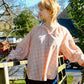 Person wearing a check shirt standing outdoors with trees and a house in the background