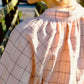 Person wearing a light pink shirt with black grid pattern outdoors